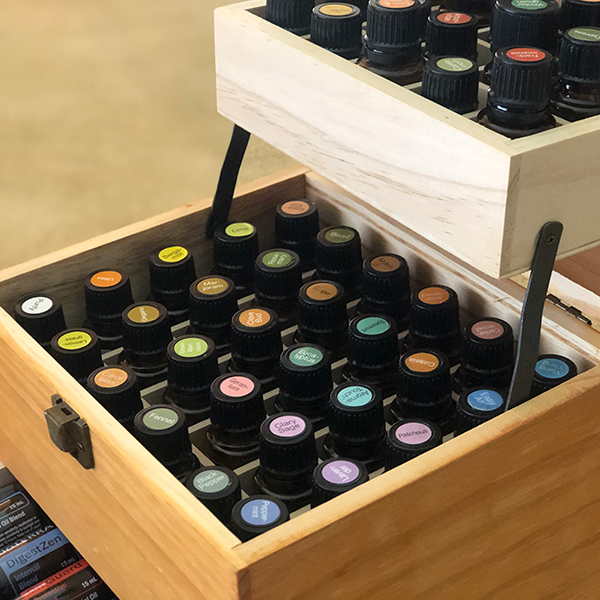 A wooden box containing various essential oil bottles with multicolored caps, each labeled differently including rose oil, displayed in a neat arrangement.
