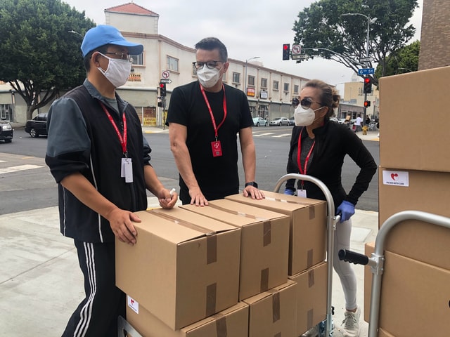 Three people wearing masks and carrying boxes on a cart, purchasing rose essential oil.