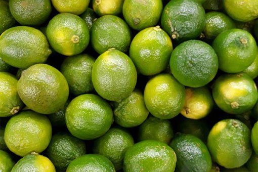 Close-up view of numerous fresh green limes filling the entire image, showing their shiny textured surfaces and emitting a Pure Lime Aroma Essential Oil - 15 ml.