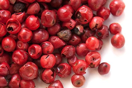 A close-up image of pink peppercorns scattered loosely, with a few showing natural blemishes against a white background, capturing the essence of Pink Pepper Essential Aromatic Oil.