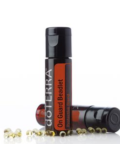 A On Guard® All Natural Softgel Beadlets bottle with the cap off, alongside several tiny beadlets, on a reflective white surface. The product label is clearly visible, emphasizing the brand and product name.