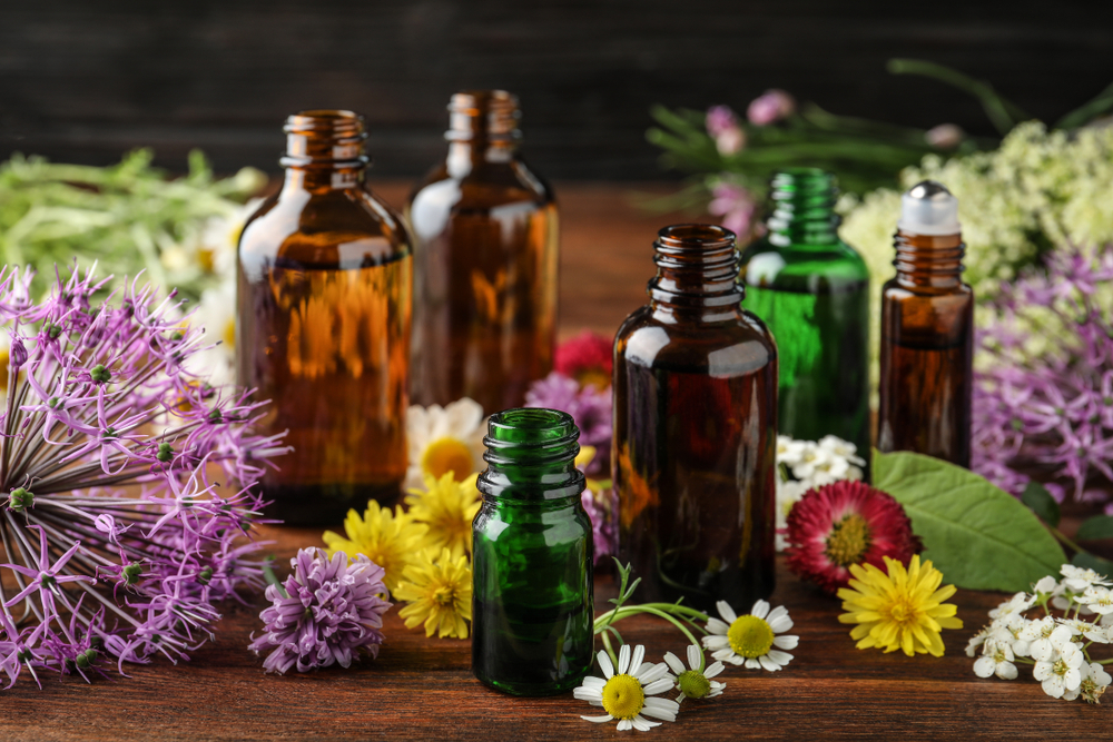 Collection of essential oil bottles on table with no lids amongst assortment of flowers
