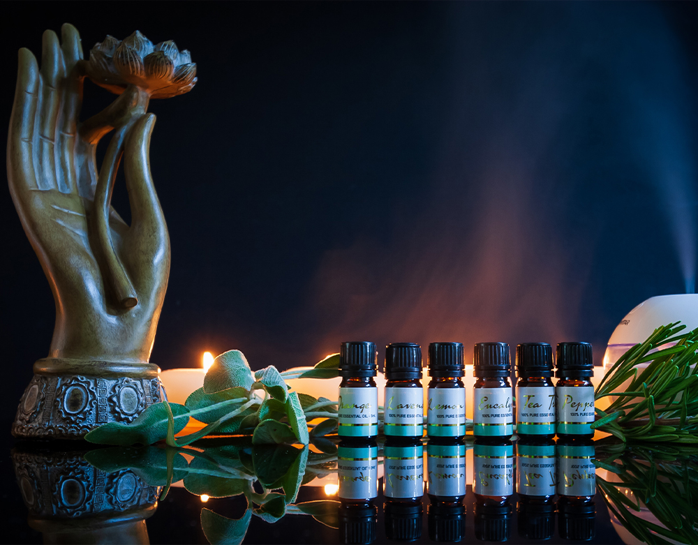 A decorative setting featuring a ceramic hand sculpture, a row of Doterra essential oil bottles, and a diffuser emitting steam, complemented by subtle lighting and green foliage.