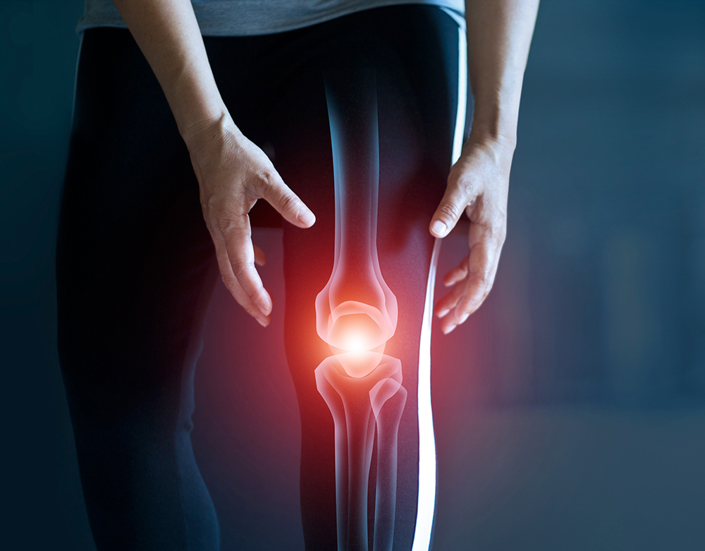 A person holds their knee, overlaid with an illustration highlighting joint pain or injury in the knee area, emphasizing the bones and inflamed spot. The image subtly incorporates rose oil, a popular choice from