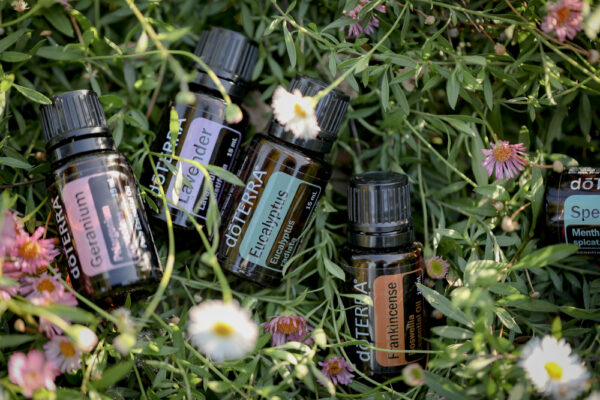 Essential oil bottles from doterra brand scattered on a bed of green leaves and pink flowers. Visible labels include geranium, spearmint, and frankincense. These are some of the best