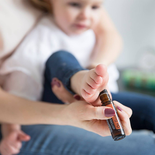 A mother applies essential oil, deemed safe for children, to the sole of her toddler's foot. The child, held in her lap, appears calm. Focus is on the child's foot and the