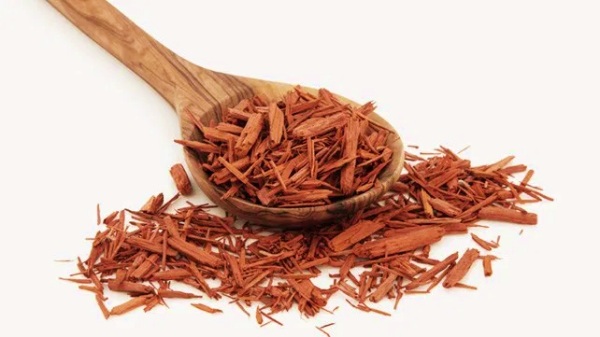 A wooden spoon filled with red sandalwood chips, infused with essential oil for sensuality, with more scattered around against a white background.