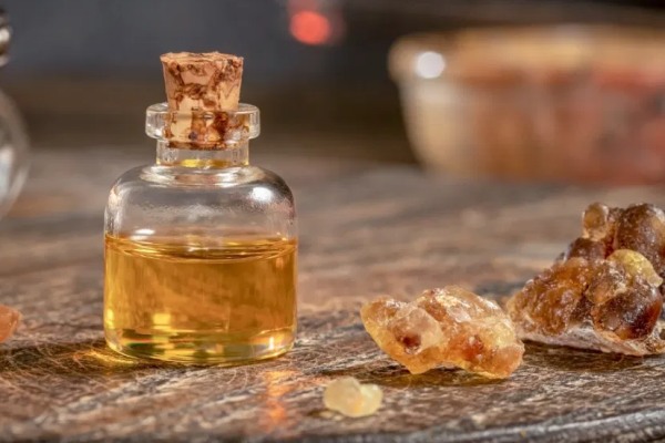 A small glass bottle with a cork stopper filled with earthsun essentials rose oil, on a wooden surface, accompanied by lumps of resin.