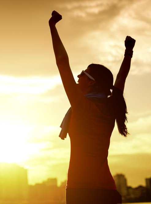 A silhouette of a woman with raised arms in victory against an earthsun backdrop, highlighting her success or achievement outdoors.