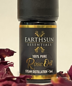 A small bottle of Rose Fragrance Oil | Perfume Oil – 100% Pure, labeled as steam distilled and containing 5ml of product, is centered and surrounded by dried rose petals.