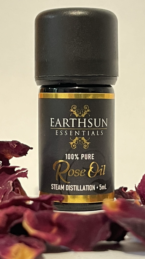 A small bottle of Rose Fragrance Oil | Perfume Oil – 100% Pure, labeled as steam distilled and containing 5ml of product, is centered and surrounded by dried rose petals.