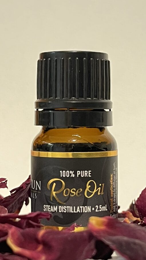 A small bottle of Rose Fragrance Oil | Perfume Oil – 100% Pure, labeled clearly, surrounded by dried rose petals. The bottle is capped with a black lid and contains 2.5ml of oil, produced