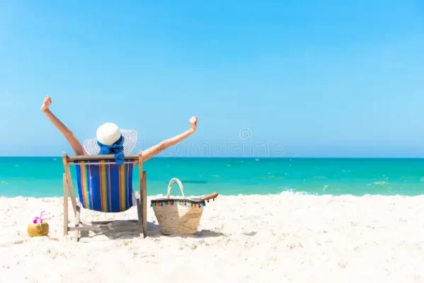 Person relaxing on a beach chair by the sea with arms raised in a carefree gesture.